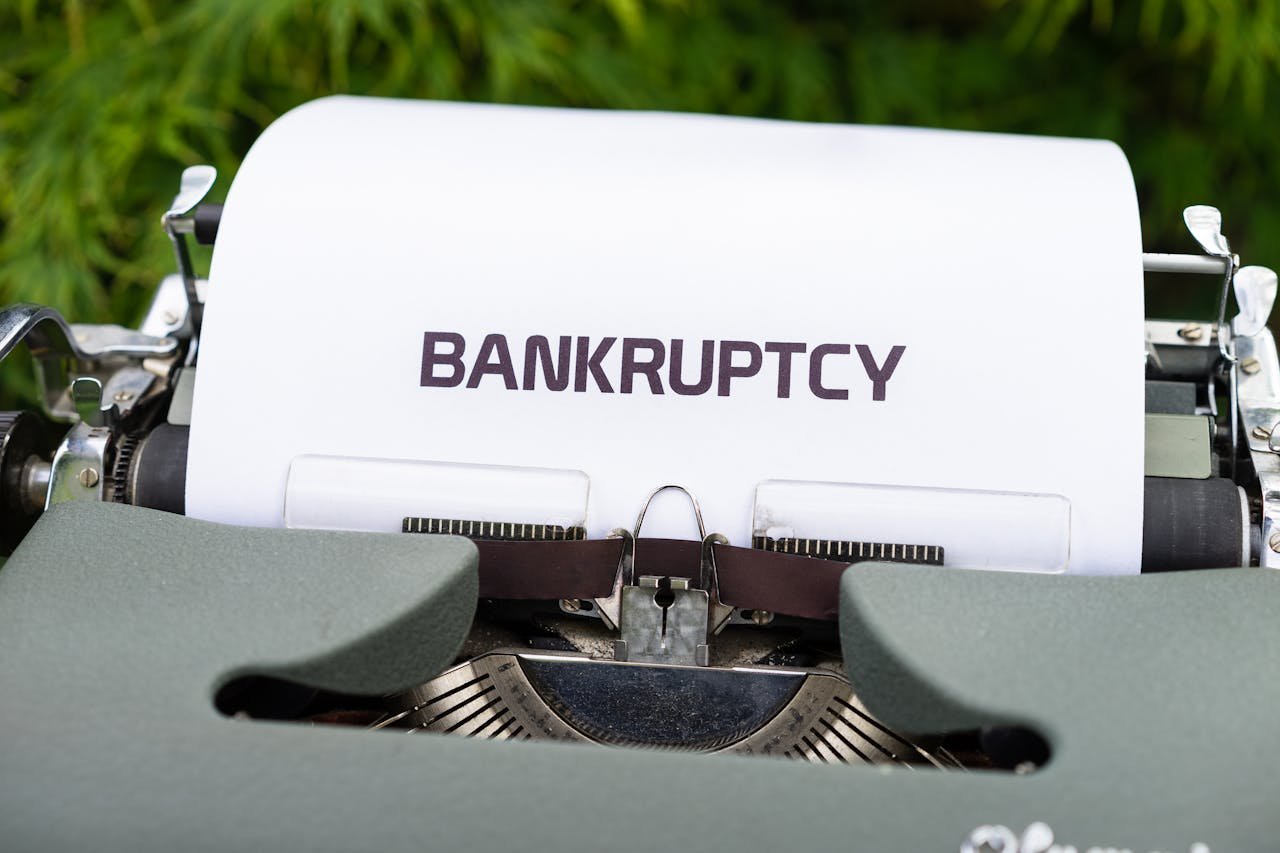 Close-up of a typewriter with the word 'BANKRUPTCY' on paper, surrounded by greenery.
